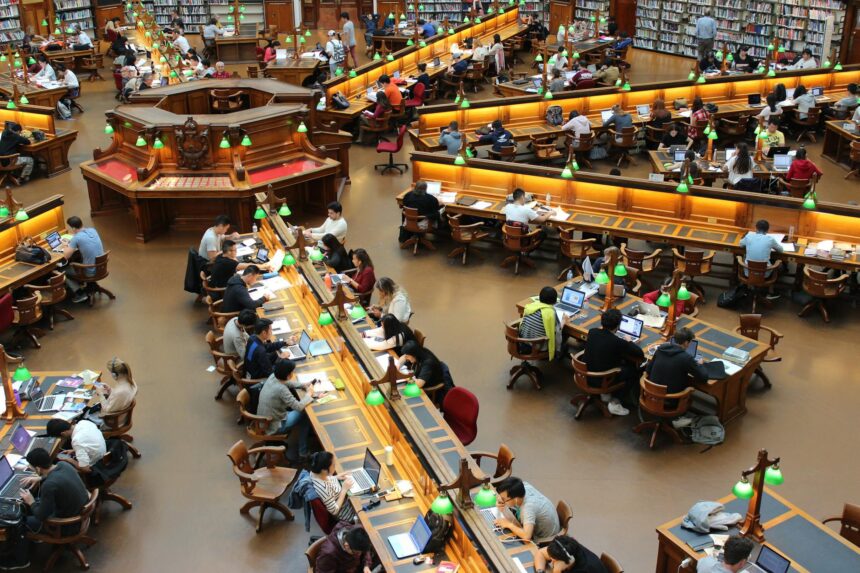 A focused college student works on their scholarship applications on a laptop in a well-lit library.