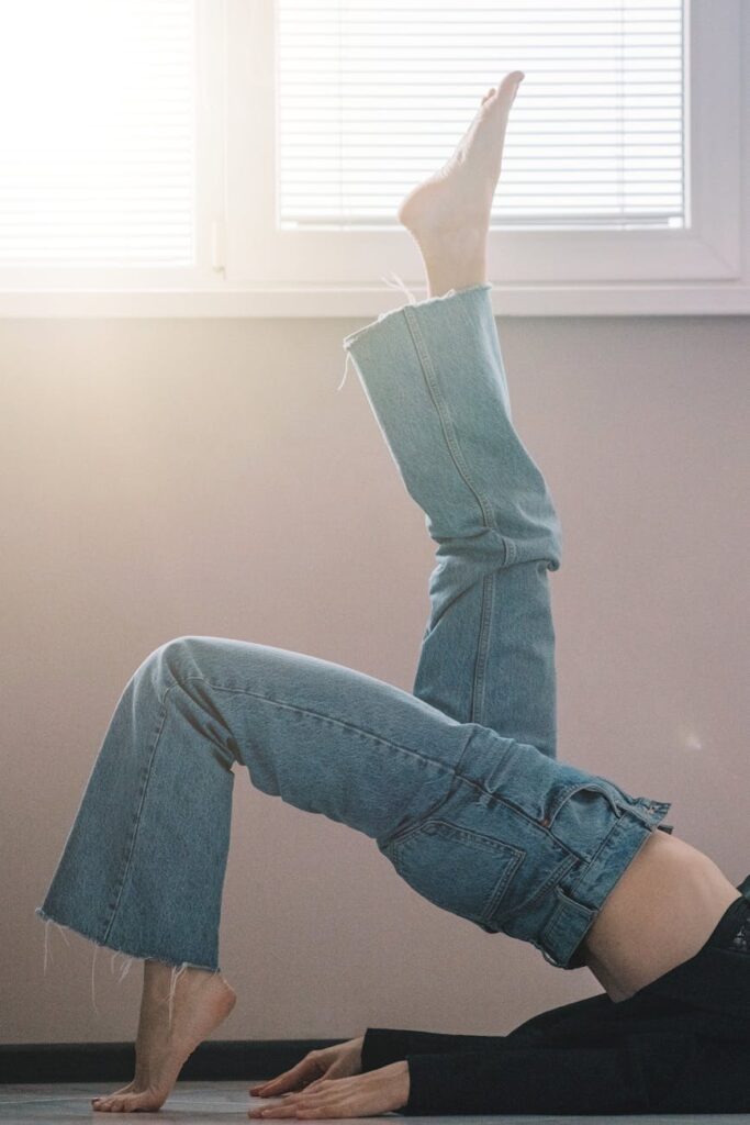 A young student in casual clothes performs a simple stretch, looking out a large window to rest their eyes.