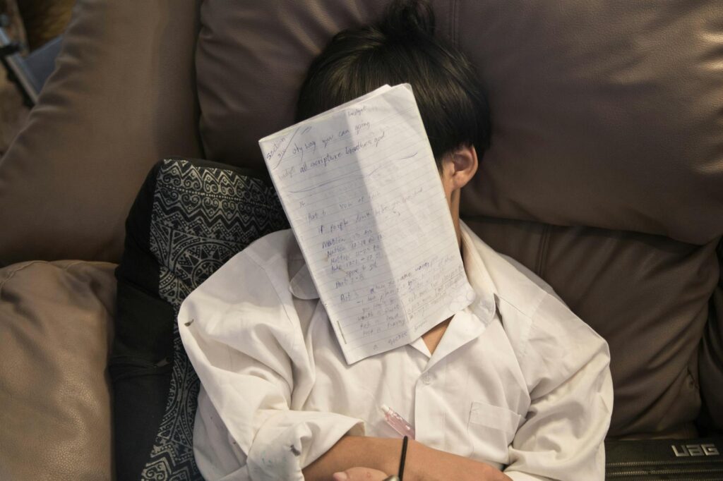 An overwhelmed student with their head in their hands, sitting in front of a large, intimidating stack of textbooks.