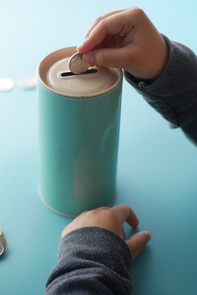 A close-up shot of a young person's hand carefully placing a golden coin into a white ceramic piggy bank, symbolizing starting to save early.