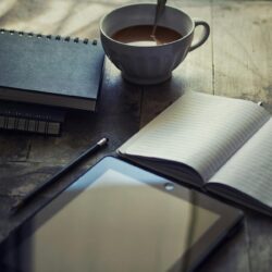 A focused student writing in a weekly planner with textbooks and a laptop nearby.