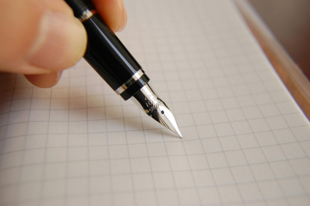 A detailed shot of a person's hand meticulously writing out a simplified explanation of a difficult concept in a spiral notebook.