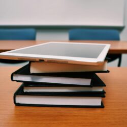 A stressed college student sits with their head in their hands in front of a large stack of textbooks and financial documents.