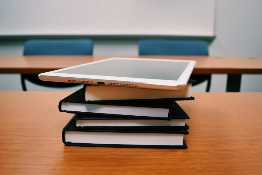 A stressed college student sits with their head in their hands in front of a large stack of textbooks and financial documents.