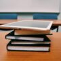 A stressed college student sits with their head in their hands in front of a large stack of textbooks and financial documents.