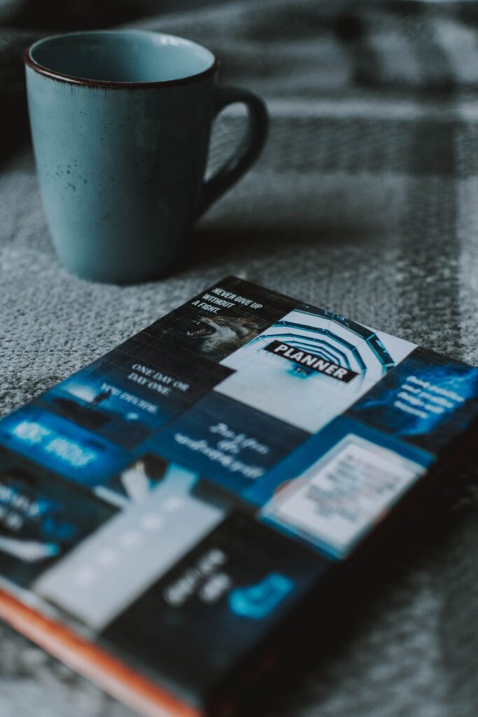 A close-up of a student's hands writing a to-do list in a daily planner next to a warm cup of tea on a desk.