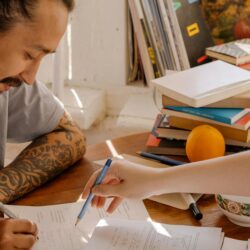 A focused college student sitting at a desk with textbooks and a small pink piggy bank, symbolizing saving money.