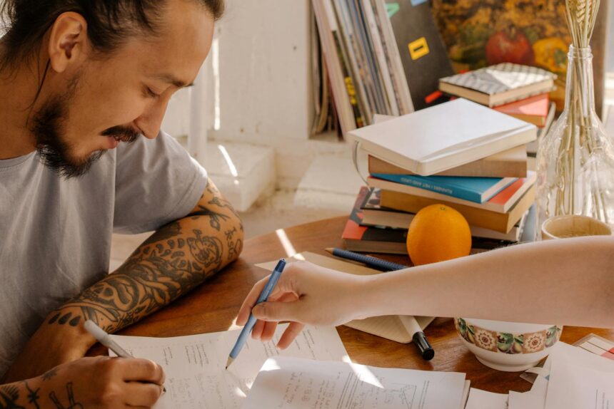 A focused college student sitting at a desk with textbooks and a small pink piggy bank, symbolizing saving money.