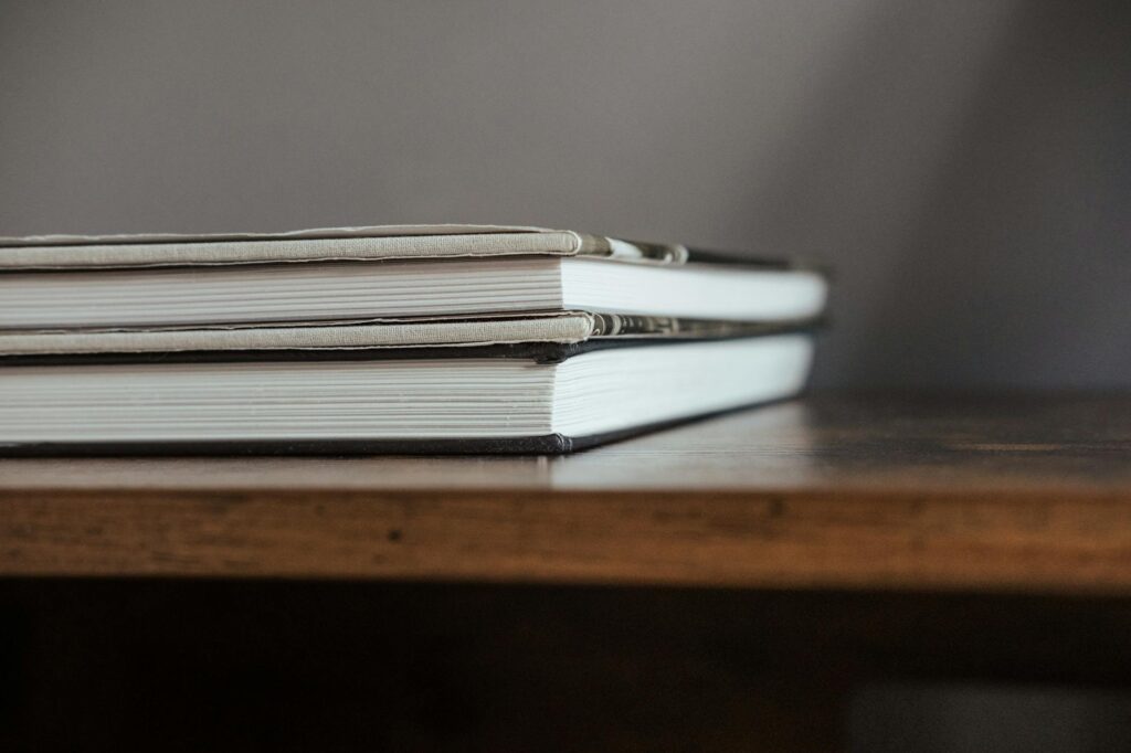 A tall stack of colorful textbooks sits on a wooden desk, symbolizing the challenge of academic study.