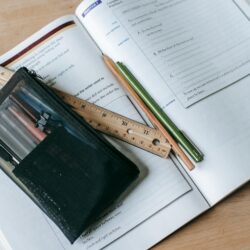 A close-up of a student's hands actively writing detailed notes in a well-used Moleskine notebook.