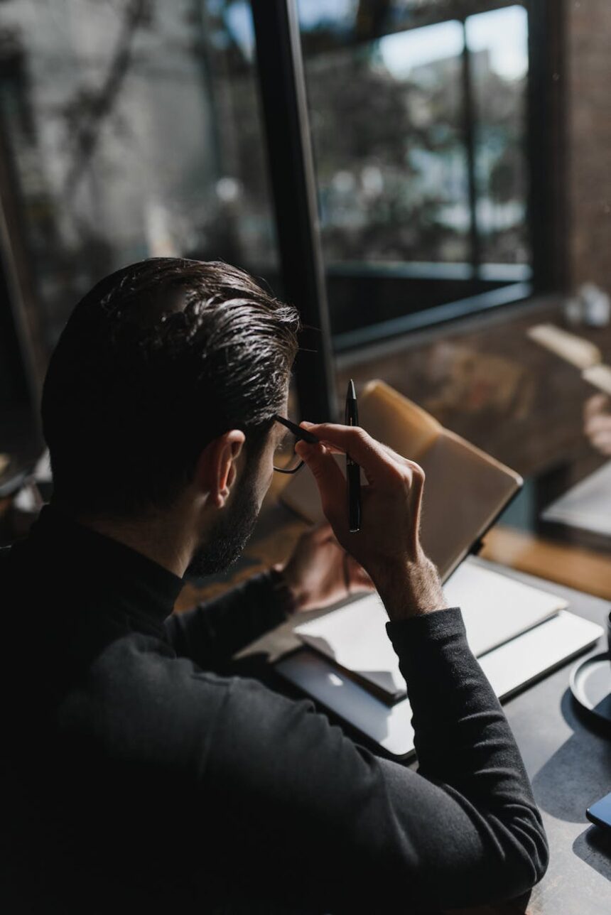 A focused student sitting at a wooden desk with a laptop and textbooks, with morning sunlight streaming through a window.