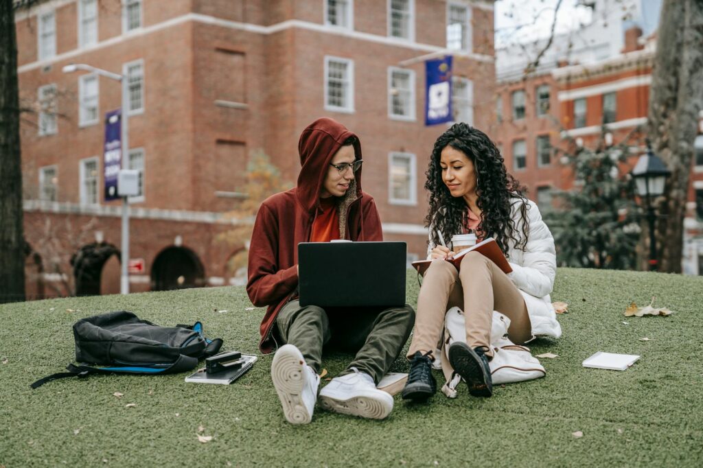 A diverse group of happy college students sitting in a circle on a sunny campus green, talking and enjoying a break between classes.