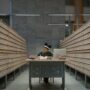 A focused university student sitting at a library desk, surrounded by stacks of books while researching grants.