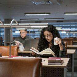 A focused student sitting at a wooden desk, surrounded by open books and highlighting notes.