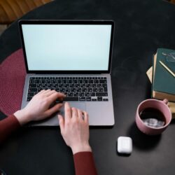 A college student with headphones on, focused on their laptop in a well-lit, modern coffee shop.
