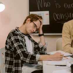 A student sits at a wooden desk, actively reviewing a stack of colorful flashcards to study for an exam.
