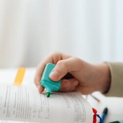 A focused student using a yellow highlighter on a key concept in a textbook, demonstrating the Pareto Principle in action.