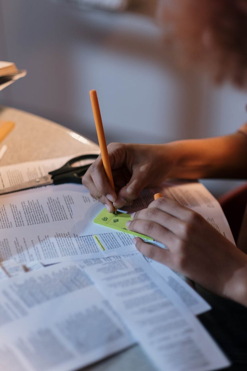 A focused student surrounded by open textbooks and a cup of coffee while studying under a desk lamp at night.