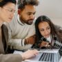 A young professional smiles with relief while working on a laptop, symbolizing the weight of student loan forgiveness.
