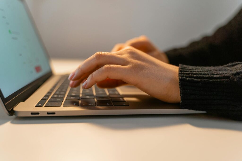 A detailed shot of a student's hands typing on a laptop, with a stack of academic textbooks visible in the background.