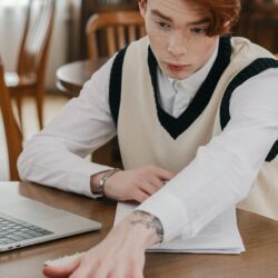 A focused student sitting at a desk covered in textbooks and using a laptop to study.