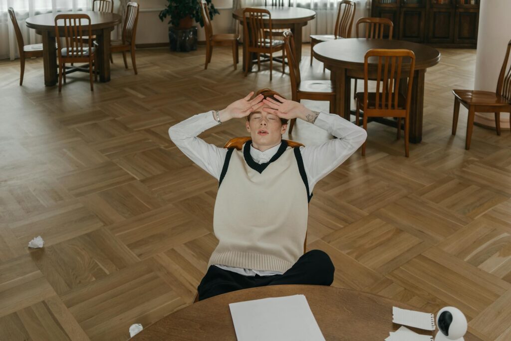 A stressed student with their head in their hands, sitting at a messy desk covered in books.