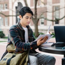 A focused college student creating a budget on their laptop in a sunlit room.