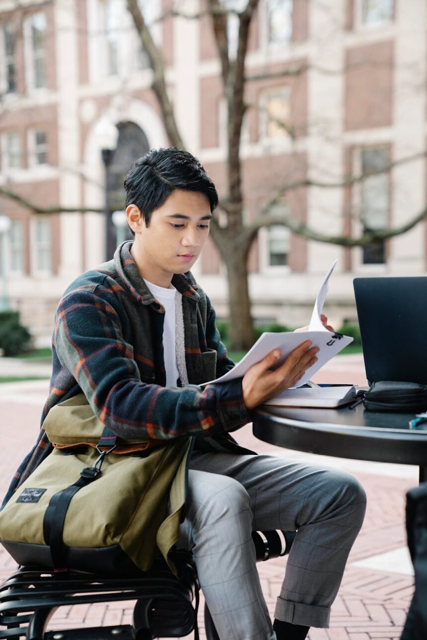 A focused college student creating a budget on their laptop in a sunlit room.
