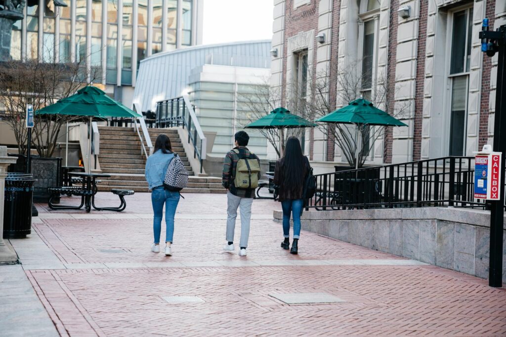 A diverse group of happy college students with backpacks walking together across a green campus quad.