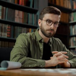 A focused student wearing headphones types on a laptop in a brightly lit university library.