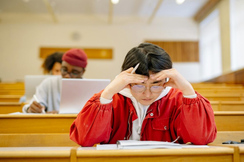 A young student wearing headphones concentrates on their laptop screen in a quiet, well-lit university library.