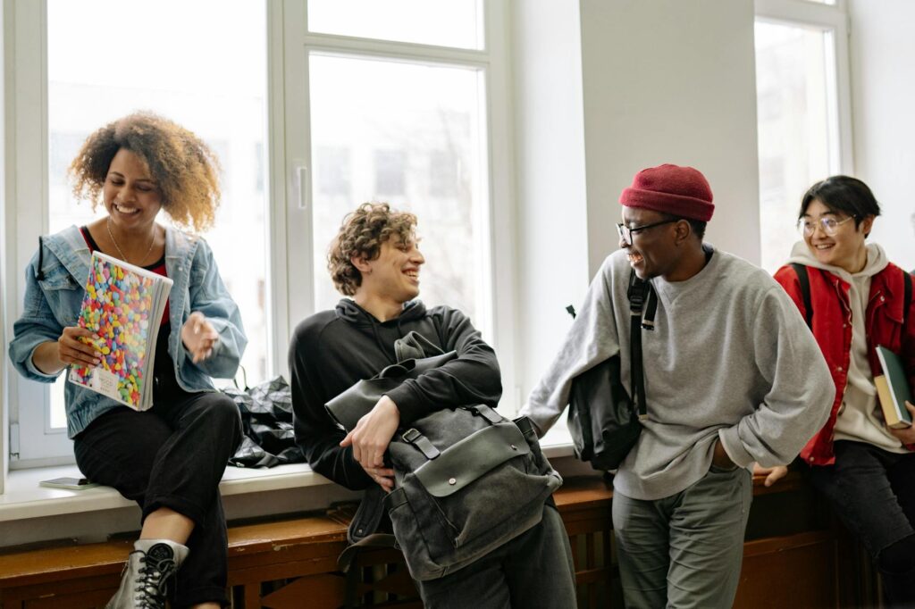 A group of four diverse students sit around a table, smiling and discussing a project together.