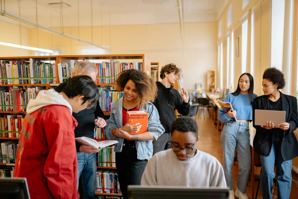 A multi-ethnic group of college students smiling and working together around a large table in a sunlit library.