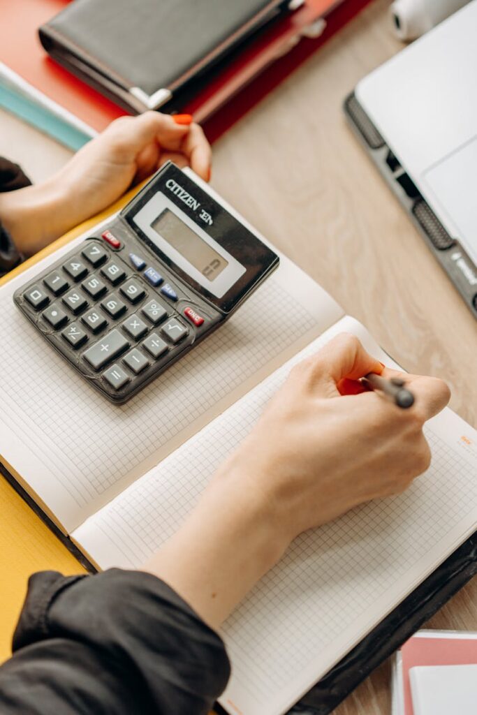 A close-up of a person's hands using a calculator and writing in a planner to create a personal budget.