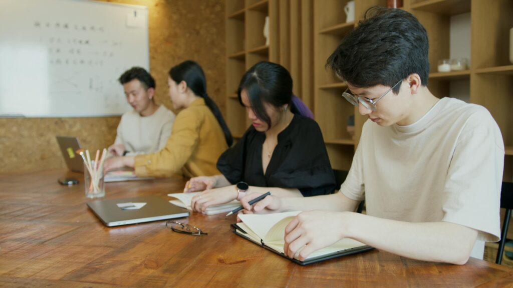 A diverse group of smiling college students sitting around a table working together on laptops.