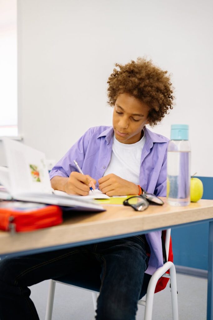 A focused student with headphones on writes diligently in a notebook in a well-lit, organized library setting.