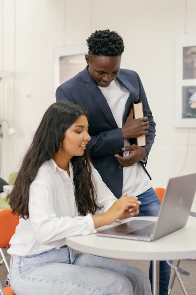A diverse group of college students working together around a table, using a laptop and tablets for a group project.