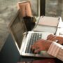 A young student diligently studying at a clean, sunlit desk with their laptop and an open notebook.