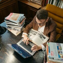 A tired college student with their head in their hands, surrounded by open textbooks and a glowing laptop screen.