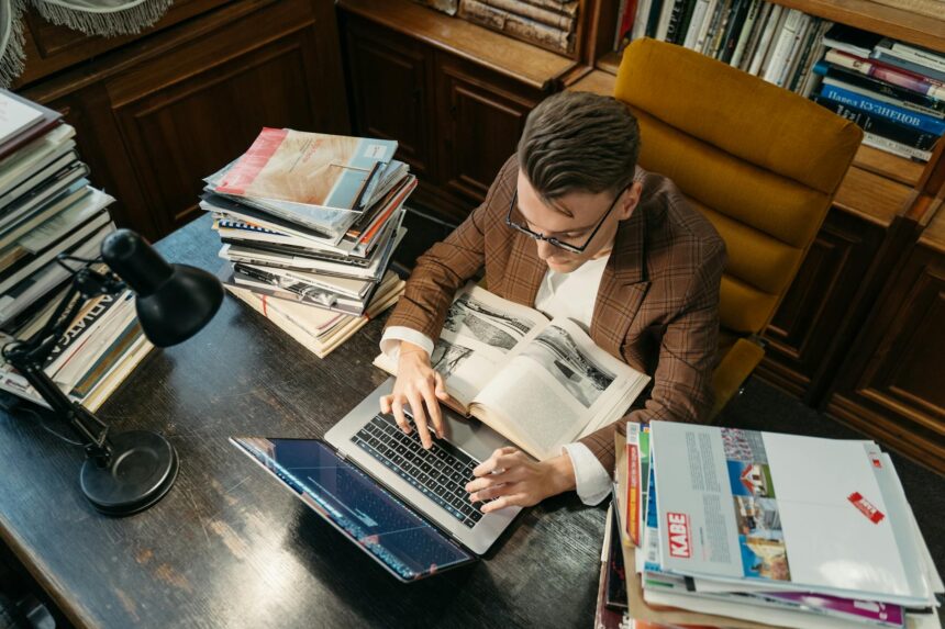 A tired college student with their head in their hands, surrounded by open textbooks and a glowing laptop screen.