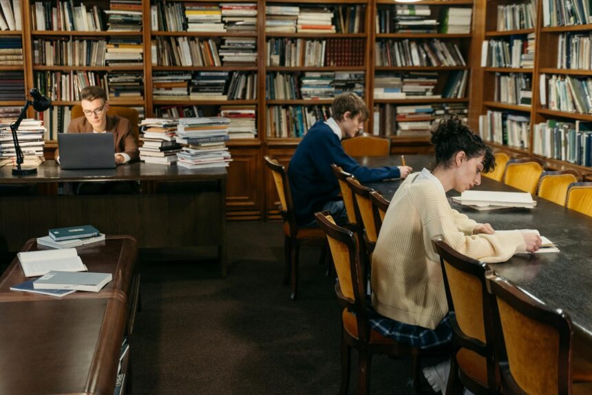 A focused student wearing headphones studies diligently at a wooden desk, surrounded by textbooks and a laptop.