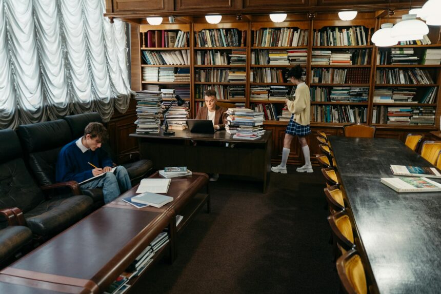 A focused student wearing headphones studies diligently at a desk covered in books and a glowing laptop screen.